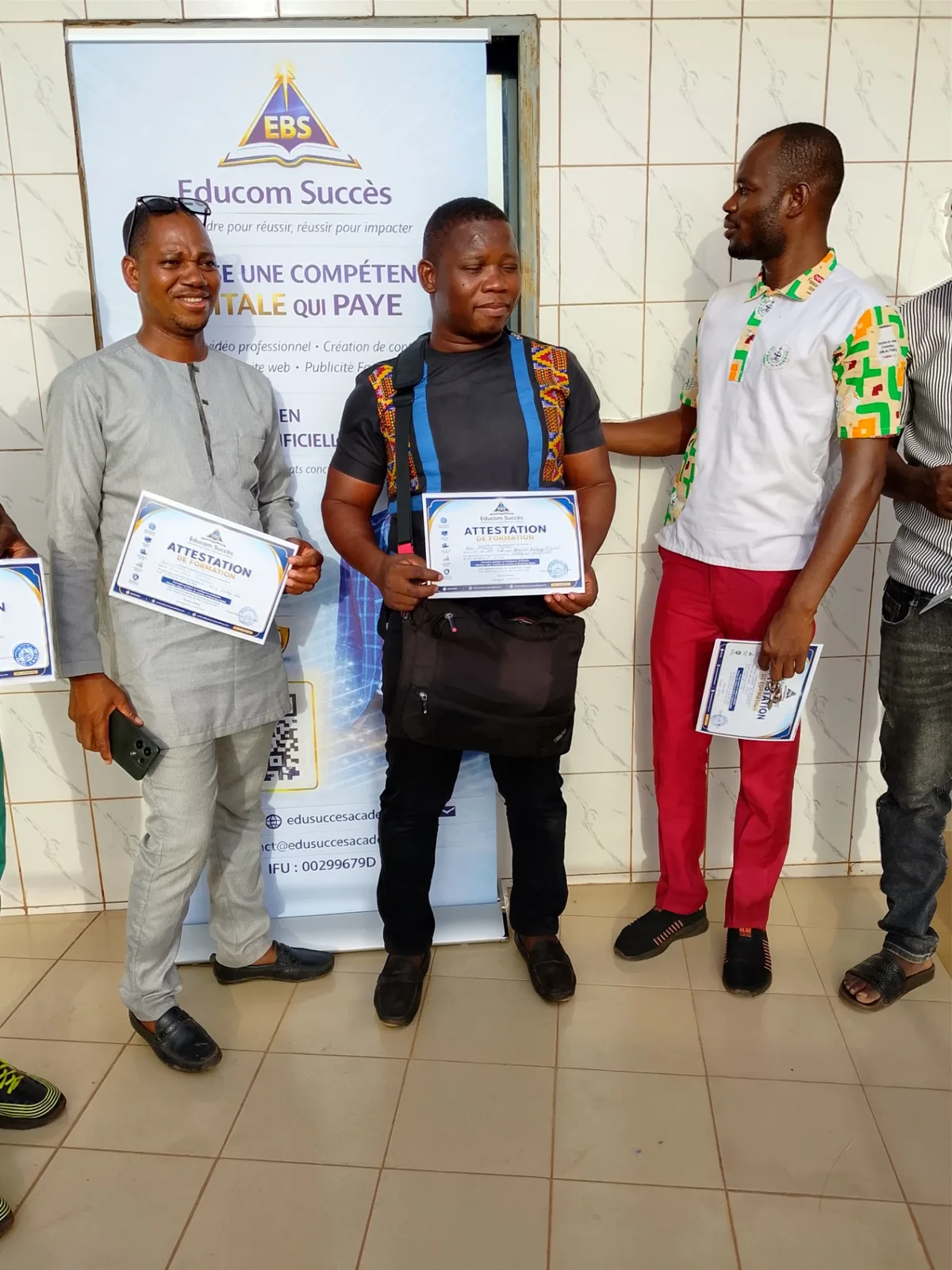 Trois participants avec leurs attestations de formation devant le kakémono Educom Succès